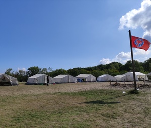 Eine Reihe Zelte auf grüner Wiese mit einer roten Fahne auf dem Dorfplatz